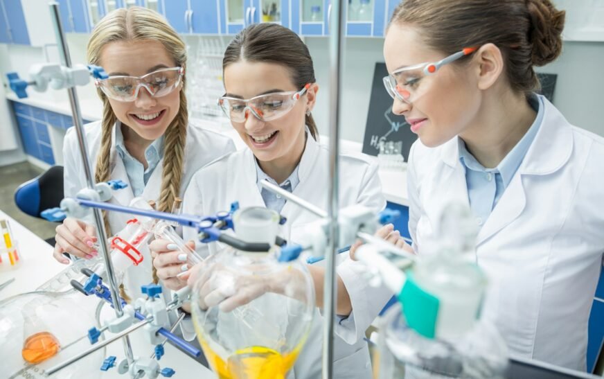 Smiling female scientists in protective eyewear making experiment in chemical laboratory