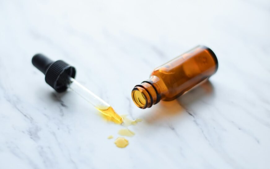 An amber bottle with a dropper and a spilled essential oil on a marble countertop