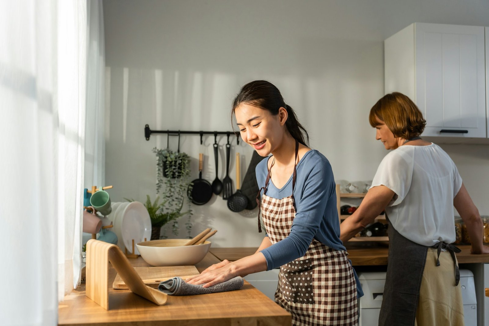 Caucasian senior elderly woman cleaning kitchen in house with daughter.